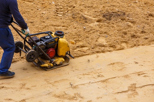 Worker using vibratory plate compactor for compaction sand during path construction. photo
