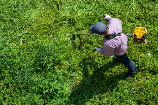 lawnmower man with string trimmer trimming grass at sunny day photo