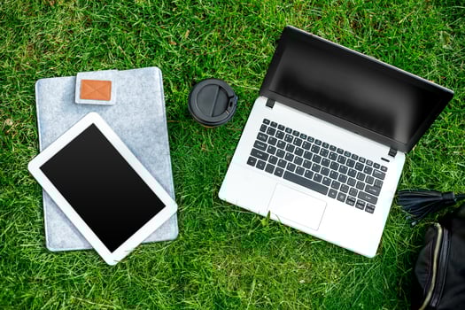 Laptop computer on green grass with coffee cup, bag and tablet in outdoor park photo