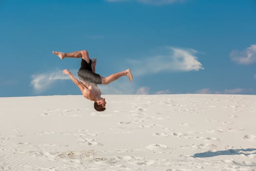 Portrait of young parkour man doing flip or somersault on the sand. photo