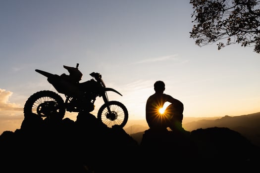 Man with motocross bike against beautiful lights, silhouette of a man with motocross motorcycle On top of rock high mountain at beautiful sunset, enduro motorcycle travel concept. photo