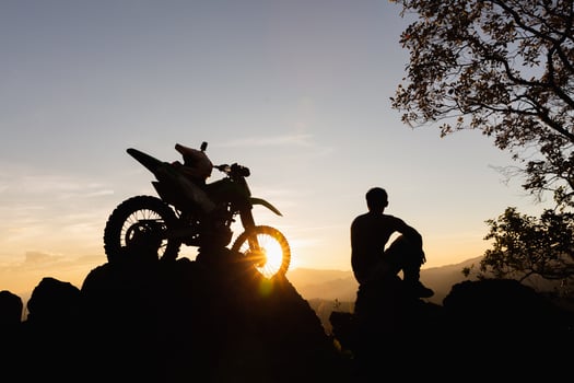 Man with motocross bike against beautiful lights, silhouette of a man with motocross motorcycle On top of rock high mountain at beautiful sunset, enduro motorcycle travel concept. photo