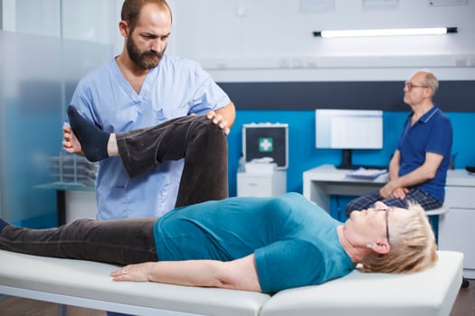 Chiropractor trying to relieve pressure from knee of old patient with arthritis and injury. Physiotherapist cracking leg bones for relief and physical recovery of senior woman with pain. photo
