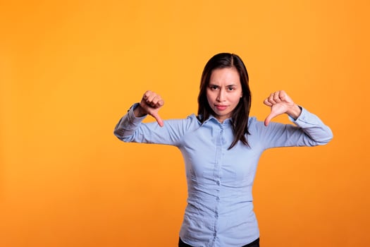 Unhappy filipino woman showing dislike gesture on camera in studio, gesturing disagreement sign with fingers. Displeased young adult expressing disapproval and disappointment sign. Dislike symbol photo