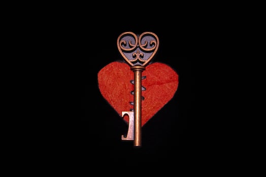 Antique old key with broken red heart on black background photo