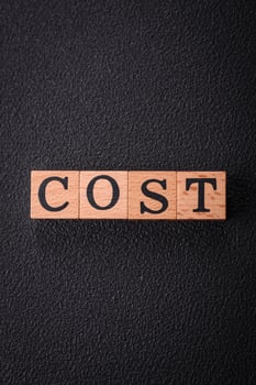 The inscription cost in wooden cubes on a dark concrete background photo
