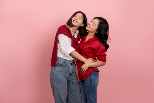 Beautiful cheerful Asian woman in a shirt and jeans is embracing and looking at the camera on a pink background. photo