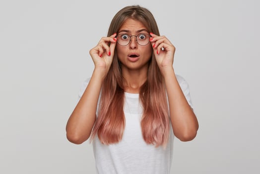 Shocked young pretty blonde woman with casual hairstyle looking confusedly at camera with wide eyes opened and holding hands on glasses, posing over white background photo
