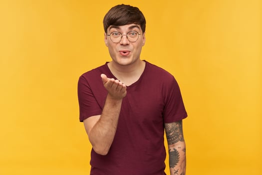 indoor shot of young pleased male, looks directly into camera and send air kiss. Isolated over yellow background photo