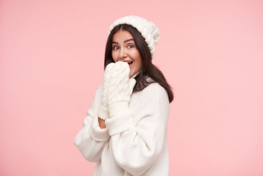 Studio photo of young agitated brunette female with natural makeup raising hands to her mouth while looking joyfully at camera, standing over pink background