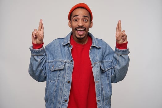 Overjoyed young pretty bearded brown haired guy with dark skin keeping fingers crossed and looking excitedly at camera with wide smile, isolated over white background photo