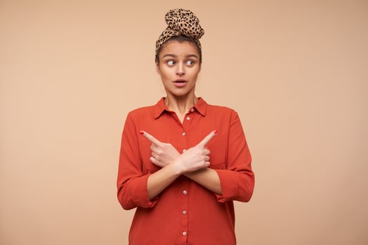Confused young pretty brown haired lady rouding her green eyes while looking amazedly aside and crossing her arms on chest, isolated over beige background photo
