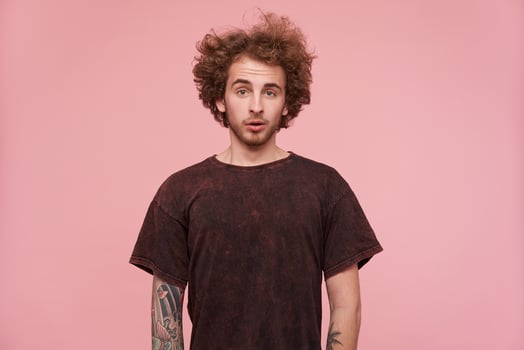 Puzlled young handsome bearded redhead man with casual hairstyle looking confusedly at camera and wrinkling his forehead, standing against pink background photo