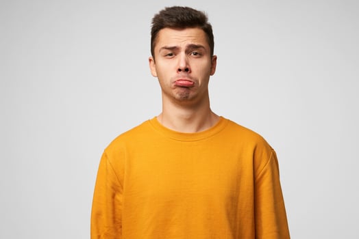 Expresses insult chilly. Portrait of emotional guy looks sad, upset, frustrated, displeased, lower lip pouted, showing defenseless, wears orange sweatshirt, stands isolated over white background. photo