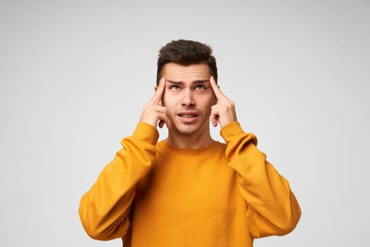 Young man ponders the idea, focused, looks up to the distance, forefingers near temples, trying to remember something, immersed in thoughts, dressed casually, isolated over white background photo