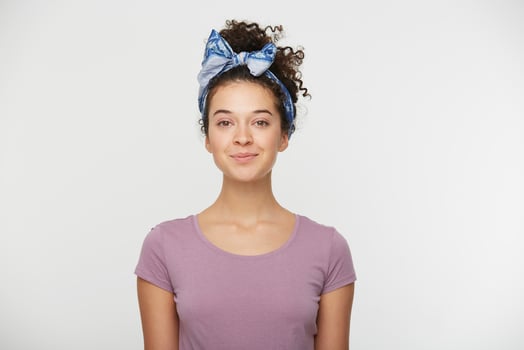 Happy female with positive expression, dressed in casual t shirt and stylish headband, poses against white background, looking at the camera with a playful smile. People and emotions photo