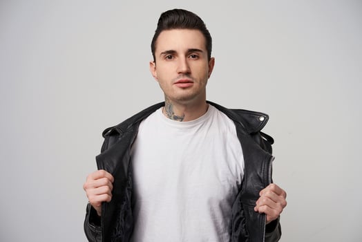 Young rebel, with a stylish haircut and styling with a briolin, tattoo on the neck, dressed in the style of 50s-60s,keeps hands like putting down black leather jacket and leaving blank white T-shirt photo