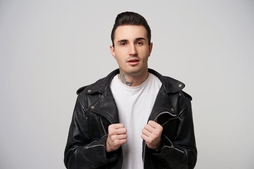 Portrait of attractive rebel, brutal with a stylish haircut and styling with a grease, tattoo on the neck,keeps hands like putting on black rocker-style leather jacket, over white background photo
