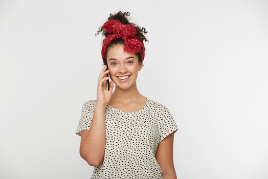 Joyful young girl shining from happiness, talking with her honey boyfriend on phone, looking happy and glad, keeps smart phone in hand, dressed white t-shirt with dots, white background photo
