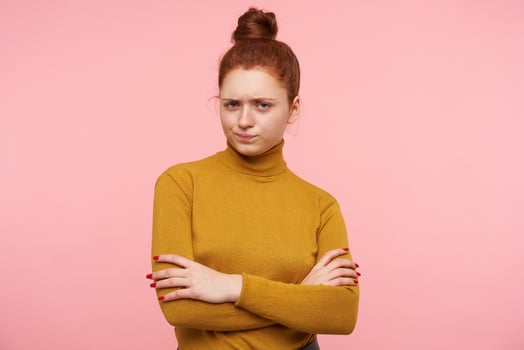 Displeased young attractive redhead woman dressed in mustard poloneck crossing hands on her chest and folding lips with pout, standing over pink background photo