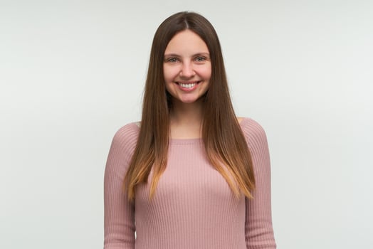 Portrait of young woman with long hair down, looks glad, smiling, dressed in a tight pink knit sweater, isolated over white background photo