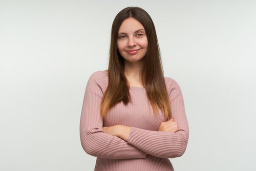 Young woman stands thoughtful, with a sly smile, considering a cunning plan, with hands crossed, looks joyful, dressed in a tight pink knit sweater, isolated over white background photo