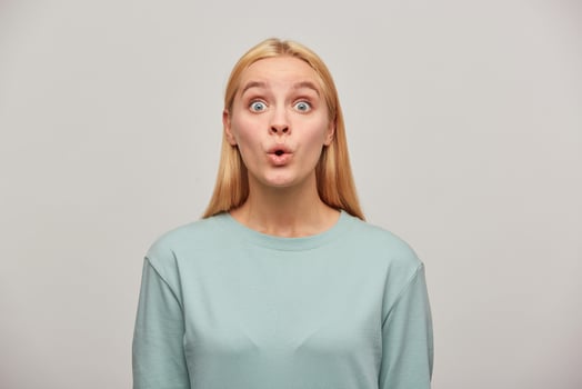 Emotional blonde young woman, looking very surprised, open-eyed, whistles in surprise, wearing blue casual sweatshirt, see something unexpected in front. Human reaction concept over grey background photo