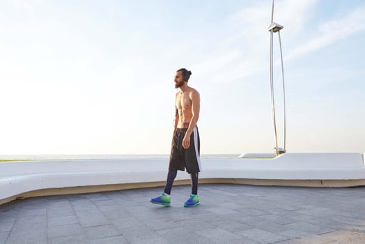 Portrait of young sporty man with beard, rest after jogging, walks at the seaside, listen favorite song on headphones. Enjoys greates morning photo
