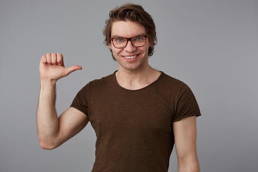 Young cool man with glasses wears in blank t-shirt standing over gray background and pointing at himself, looks cheerful and broadly smiles. photo