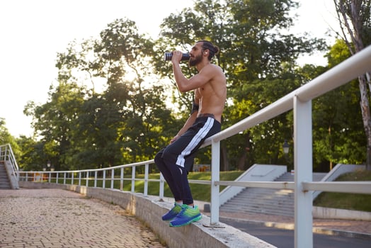 Young attractive bearded guy has extreme sport in park, rest at the park after jogging, drinking water, leads healthy active lifestyle. Fitness male model. photo