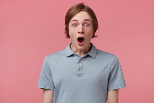 Portrait of young man with shocked, amazed expression and dropped jaw dressed in polo t-shirt isolated on pink background photo