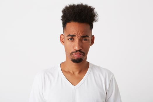 Portrait of sad upset african american young man with curly hair wears t shirt looks depressed and curving lips isolated over white background photo