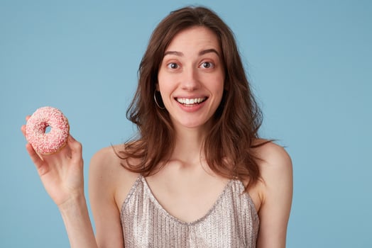 Young european woman going to eat sweet pink donut holds it in hand, over isolated blue background, amazed, very excited, cheering happy emotion photo