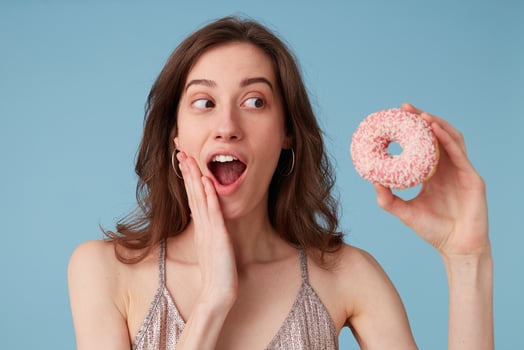 Young european woman looking aside with surprise, going to eat sweet pink donut holds it in hand, over isolated blue background, amazed, very excited, cheering happy emotion photo
