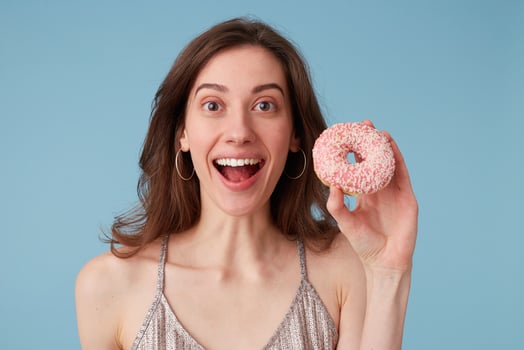 Young european woman eating sweet donut holds it in hand, over isolated blue background, screaming, very excited, cheering emotion photo