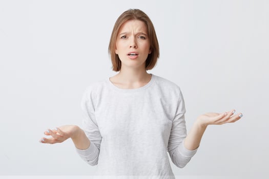 Portrait of confused upset young woman in long-sleeve looks puzzled and holding copy space on both palms isolated over white background photo