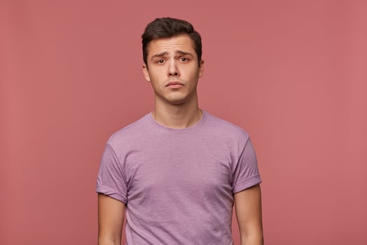 Portrait of young attractive boy in blank t-shirt, stands over pink background and looks sad and unhappy. photo