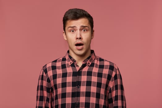 Young handsome amazed man in checkered shirt, looks at the camera with with wide open mouth in surprised expression, isolated over pink background. photo