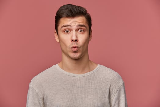 Portrait of handsome young cheerful man wears in blank long sleeve, looks at the camera with happy expressions,sens kiss, stands over pink background. photo