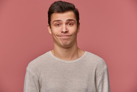 Portrait of handsome young sad man wears in blank t-shirt, looks at the camera with with mistrust, stands over pink background. photo