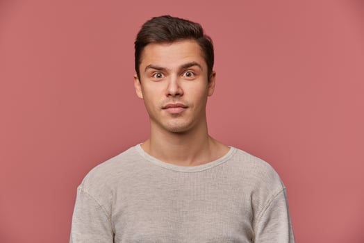 Young attractive man in blank longsleeve, calmly looks at the camera, stands over pink background. photo
