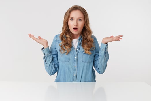 Portrait of young wondered cute curly blonde lady in denim shirts sitting at the white table and spreads his arms to the side, isolated over white background. photo