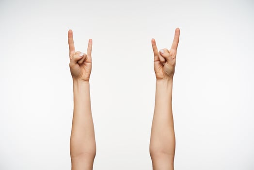 Close-up of young woman's hands showing heavy metal and rock gesture while posing against white background. Body language and signs concept photo