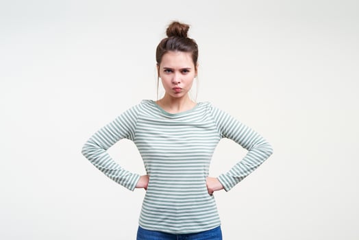 Serious young attractive brunette woman with casual hairstyle looking crossly at camera and keeping hands on her waist while posing over white background photo