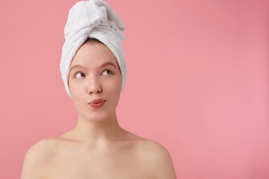 Close up of thinking young woman with a towel on her head after shower, looks away and dreams about new dress, stands over pink background. photo