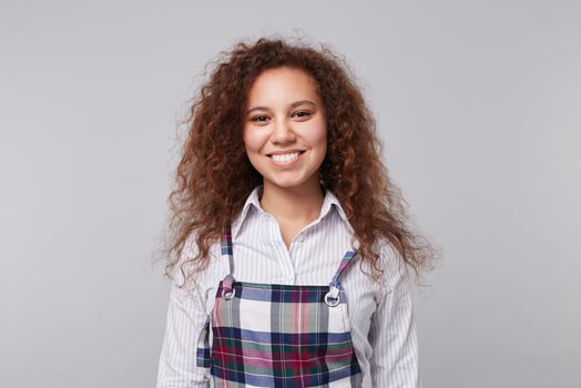 Cheerful young lovely long haired curly brunette woman showing her white perfect teeth while smiling happily at camera, standing over grey background photo