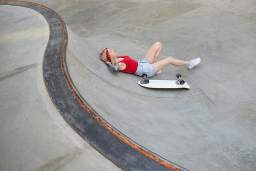 Outdoor shot of beautiful tattooed female in jeans shorts and red top relaxing over skate park on warm summer day, having break after skating photo