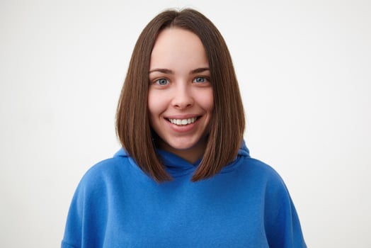 Closeup of young glad lovely short haired brunette female without makeup looking cheerfully at camera with wide smile while posing over white background photo