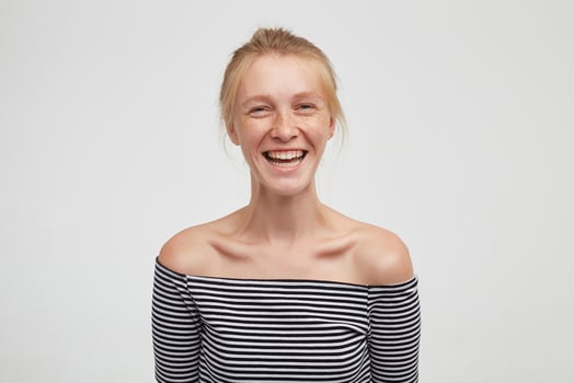 Joyful young beautiful woman wearing her foxy hair in knot while standing over white background with hands down, looking happily at camera with wide sincere smile photo