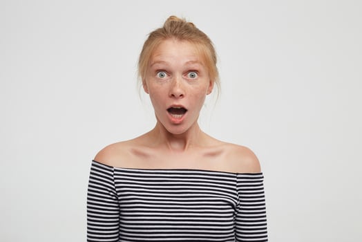 Shocked young pretty redhead woman with bun casual hairstyle looking amazedly at camera with wide eyes and mouth opened, isolated over white background photo